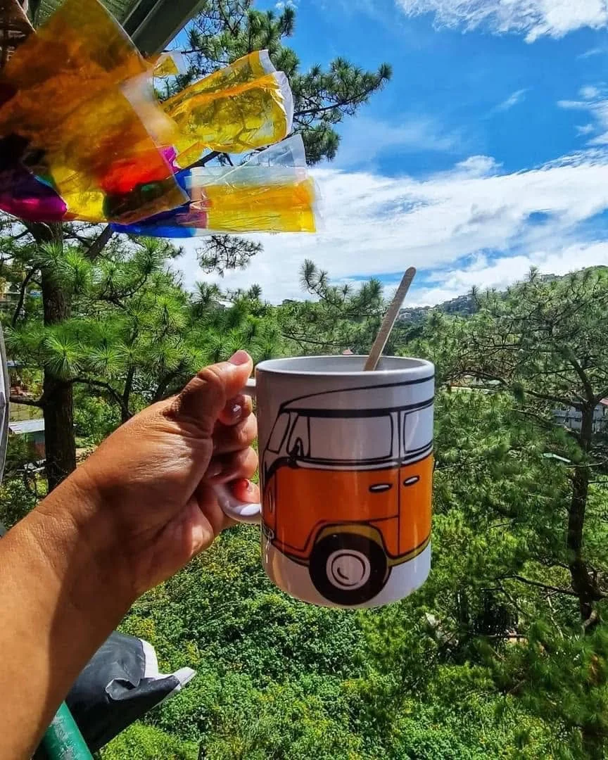 Volkswagen-themed mug held in front of pine trees